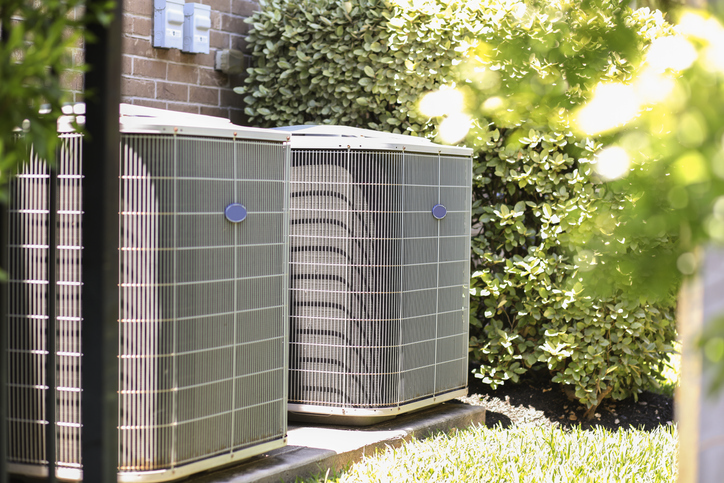 Air conditioner unit outdoors in side yard of a brick home in hot summer season. | Advanced Heating and Air Conditioning
