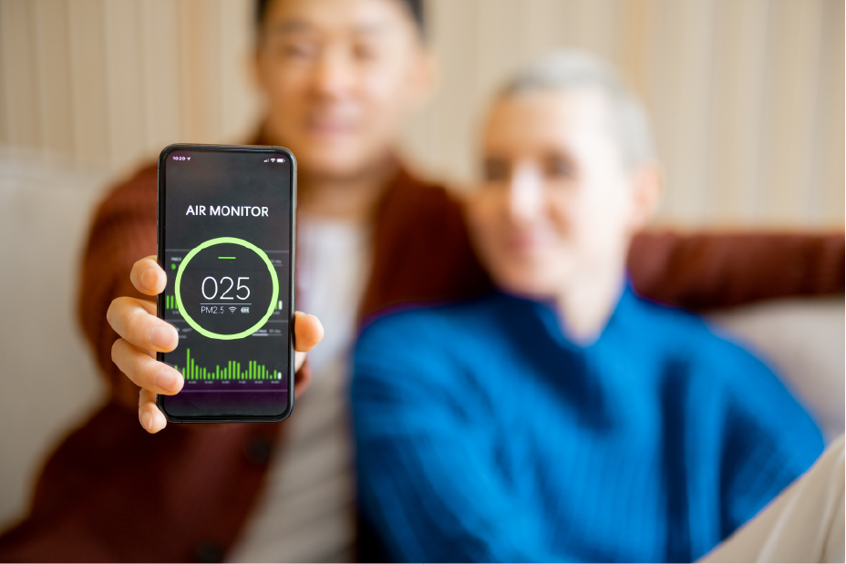man sitting on sofa with his wife and showing smartphone with home air condition app. | Advanced Heating and Air Conditioning