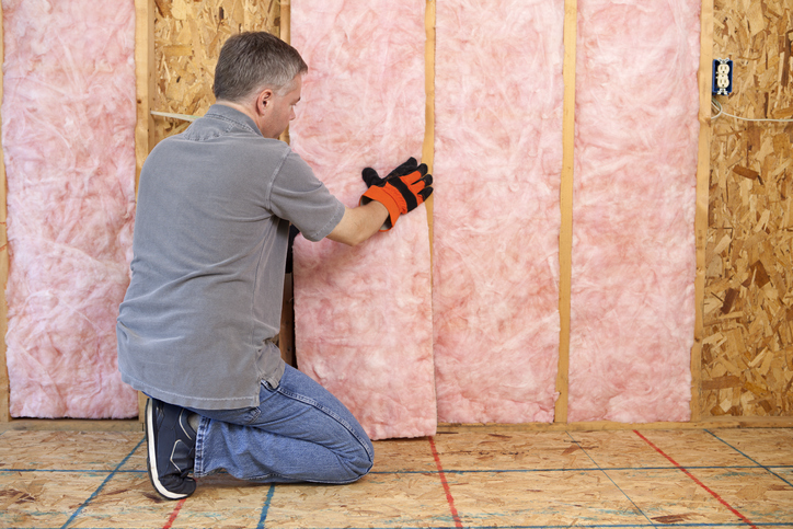 Man installing fiberglass insulation in the wall | Advanced Heating and Air Conditioning