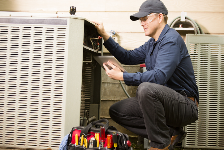 Repairmen works on a home's air conditioner unit outdoors. | Advanced Heating and Air Conditioning